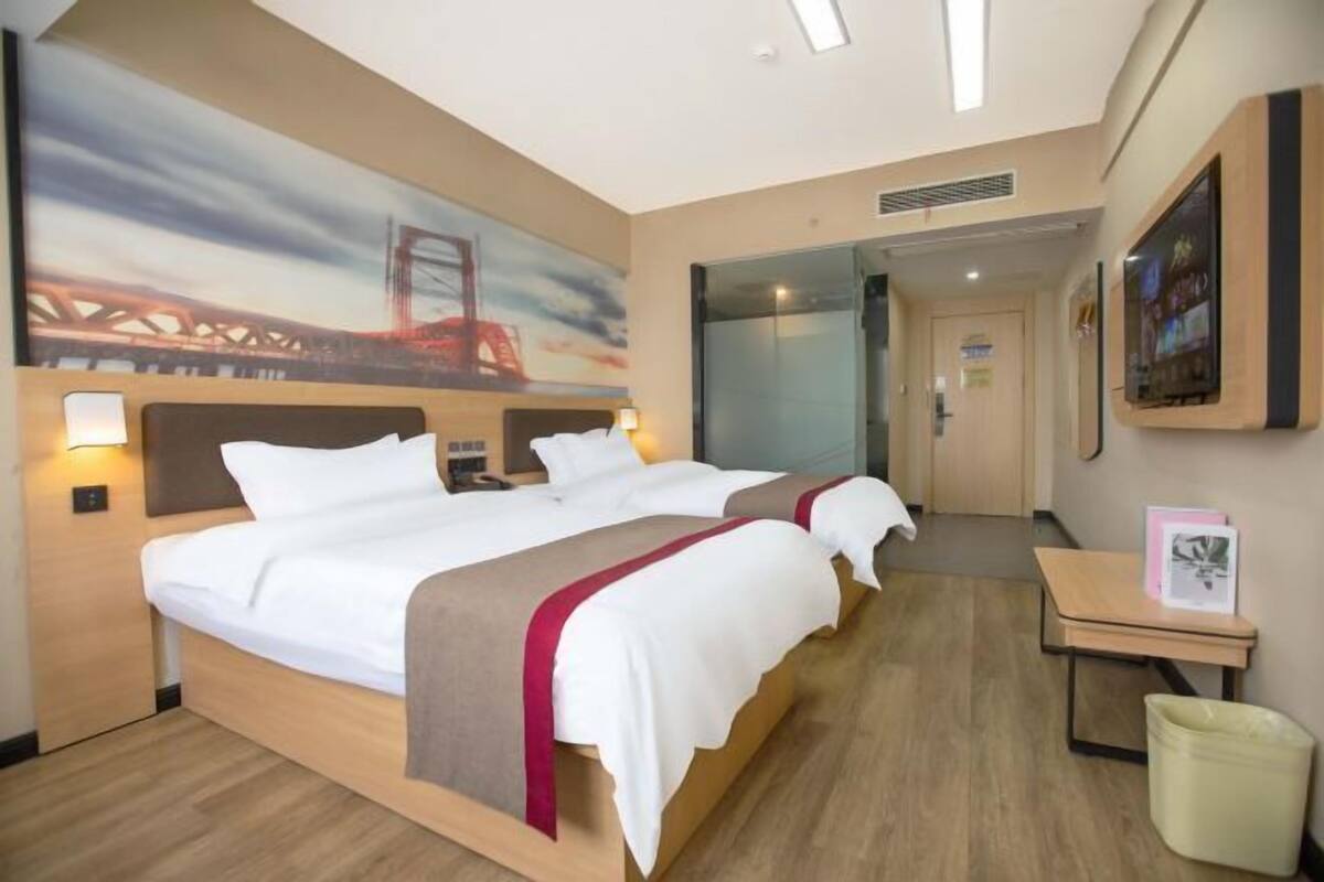 A hotel room with a large bed, a bedside table, a trash bin, and a painting on the wall.