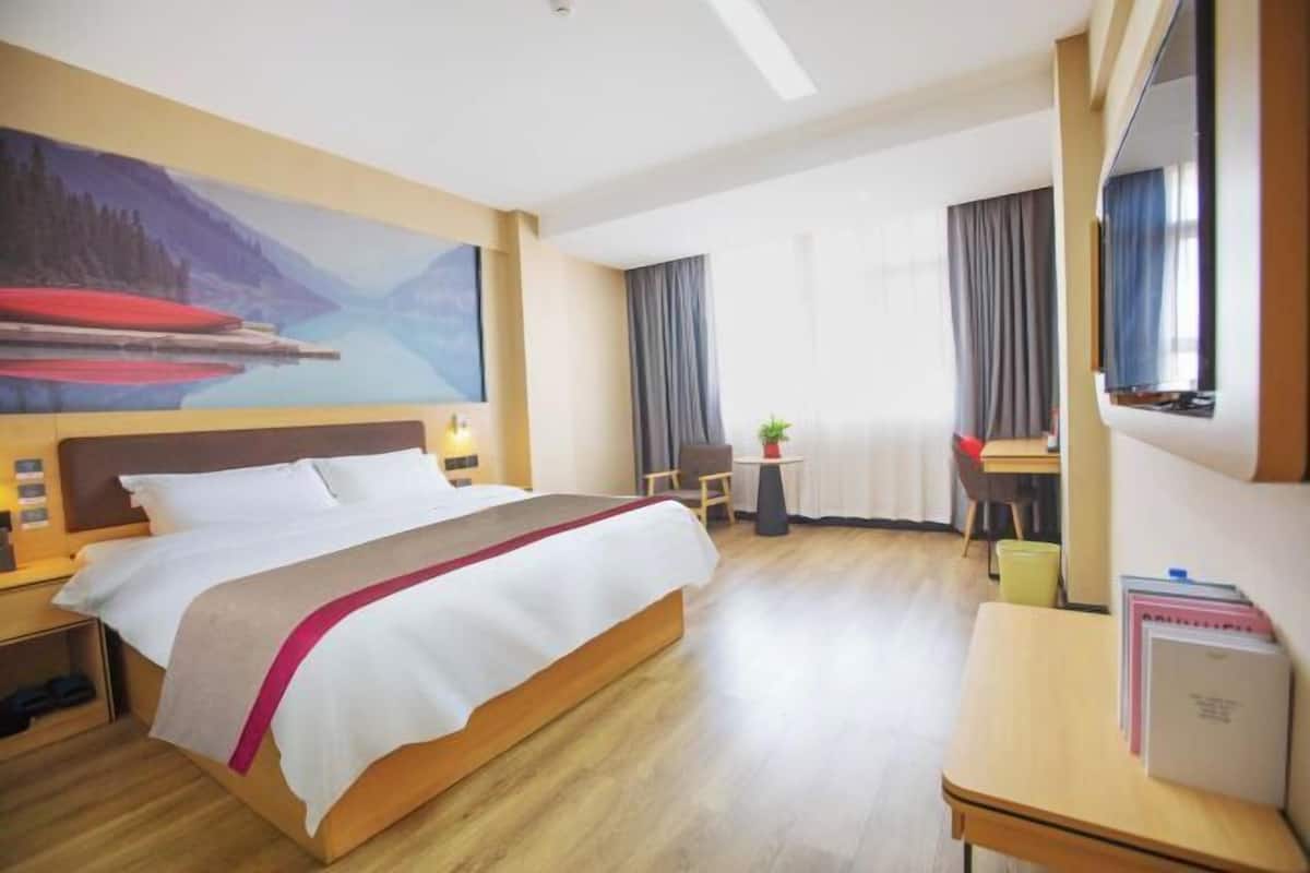 A hotel room with a large bed, a desk, a chair, a small table, and a painting on the wall.