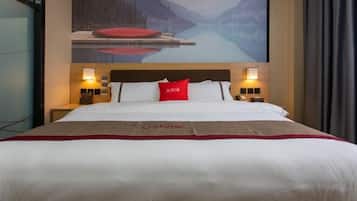 Habitación de hotel con una cama grande, un almohadón rojo y un cuadro de un lago y montañas en la pared.