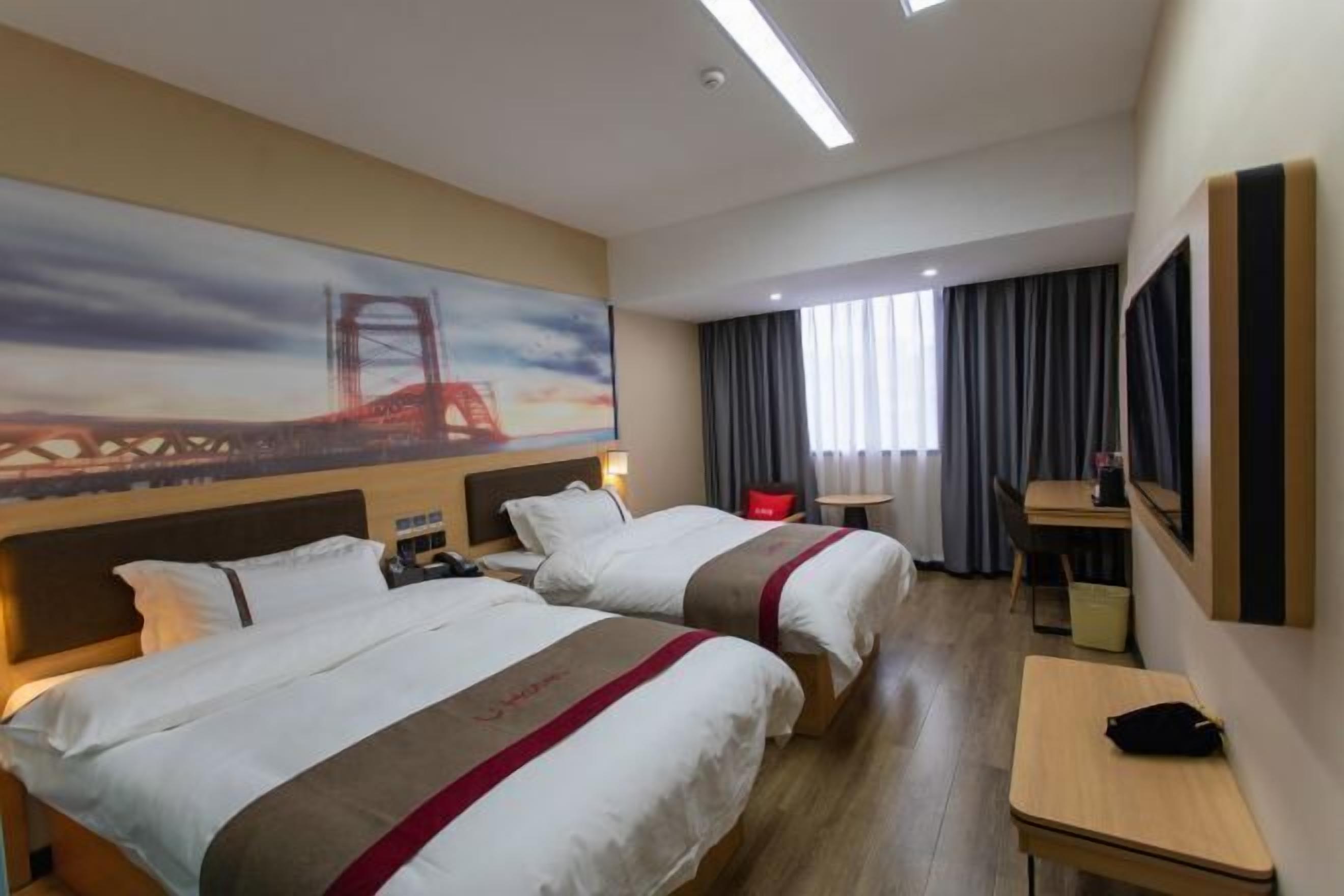 A hotel room with two beds, a desk, a chair, a TV, and a painting of a bridge.