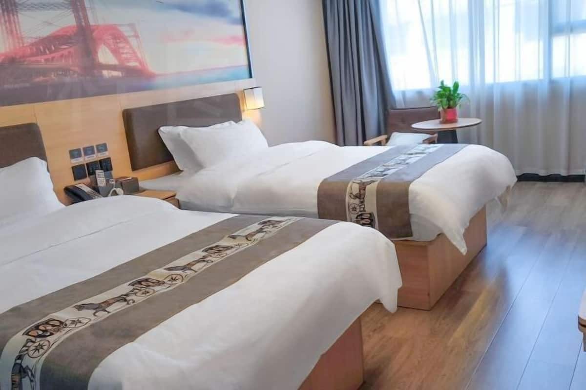 A hotel room with two beds, a small table with a plant, a painting on the wall, and a wooden floor.
