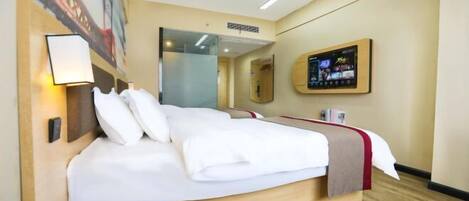 A hotel room with a large bed, a bedside table, a wall-mounted TV, and a painting on the wall.