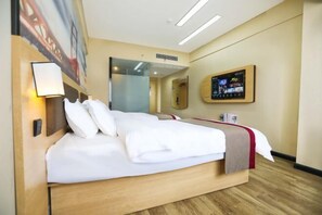 A hotel room with a large bed, a bedside table, a wall-mounted TV, and a painting on the wall.