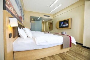 A hotel room with a large bed, a bedside table, a wall-mounted TV, and a painting on the wall.