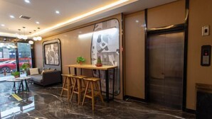 A modern lobby with a marble floor, a seating area with stools, a small table with a plant, and an elevator. - Thank U Hotel (Lengshuijiang Red Double Happiness Building Material Market) (Lengshuijiang)