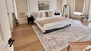 Une chambre à coucher comprenant un lit, un ventilateur de plafond, une table de chevet, une commode, un tapis et une fenêtre avec des stores.