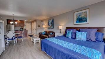 A hotel room with a large bed, a sitting area with a sofa and a small table, a kitchenette, and a dining area with a round table and chairs.