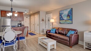 A modern living room with a brown leather sofa, a dining table with chairs, a white coffee table, and a kitchen area with wooden cabinets and a refrigerator. - Basecamp for Your Mountain Adventure (Durango)