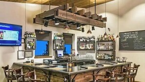 A bar area with a wooden bar counter, multiple stools, and shelves stocked with bottles. - Basecamp for Your Mountain Adventure (Durango)