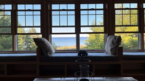 A room with a large window seat overlooking a body of water, a table with a candle holder, and a stack of books. - Lake Michigan/Beaver Island with incredible private beach (Beaver Island)