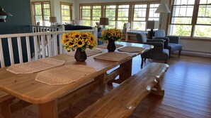 A wooden dining table with woven placemats and sunflowers, set in a room with large windows and striped chairs. - Lake Michigan/Beaver Island with incredible private beach (Beaver Island)