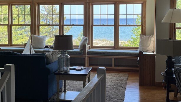 A living room with a view of the sea, wooden furniture, and a lamp. - Lake Michigan/Beaver Island with incredible private beach (Beaver Island)