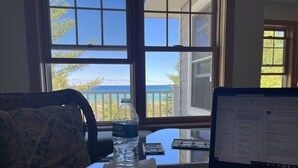 A laptop on a glass table with a calculator and a water bottle, a patterned sofa, and a view of the ocean through large windows. - Lake Michigan/Beaver Island with incredible private beach (Beaver Island)
