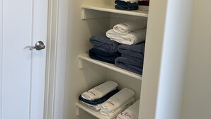 Een witte kast met planken vol met gevouwen handdoeken in verschillende kleuren.
