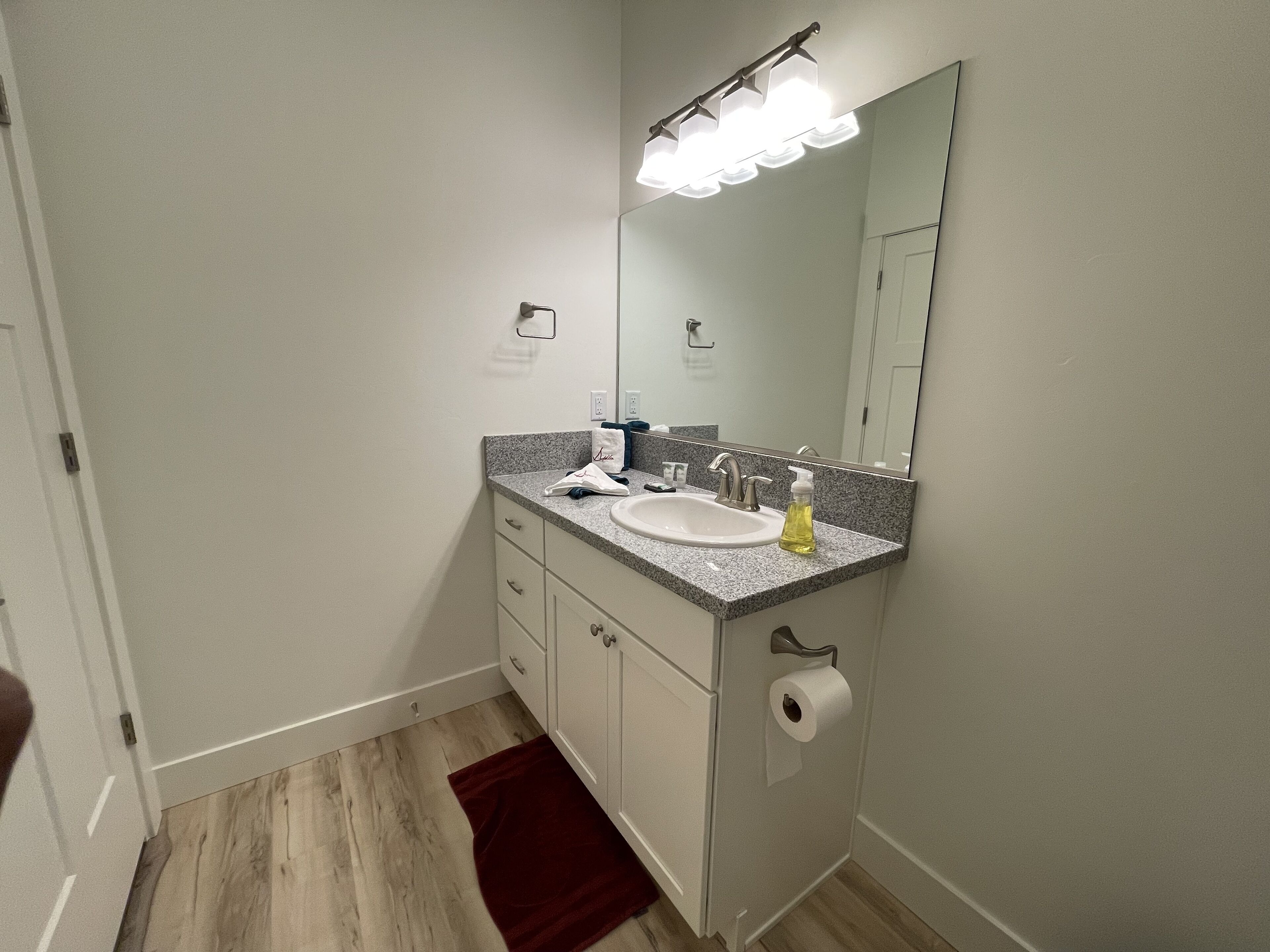 A bathroom with a white sink, a mirror, a towel, and a red rug.