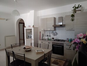 Una cocina moderna con una mesa de comedor, sillas, microondas integrado, cocina a gas y utensilios colgantes.