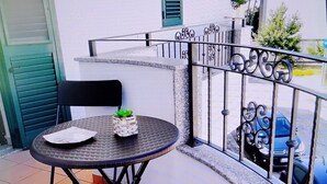 Un petit balcon extérieur avec une table ronde, une chaise et un pot de fleurs.
