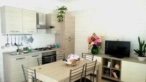 Une cuisine compacte dotée d’appareils électroménagers modernes, une table à manger avec des chaises, un téléviseur et une bibliothèque.