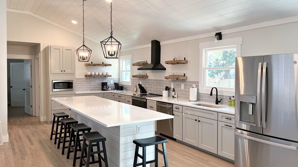 A modern kitchen with a large island, stainless steel appliances, and bar stools. - Coastal Cottage in Charming Old Mt Pleasant! (Mount Pleasant)