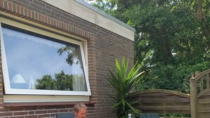 Un homme est assis sur une chaise devant un bâtiment dont le mur est en briques et qui possède une grande fenêtre.
