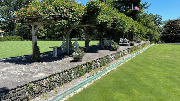 Een goed onderhouden golfbaan met een pad van natuursteen, houten pergola’s en zitplaatsen.