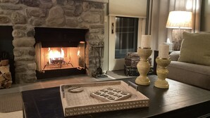 Een woonkamer met een stenen open haard, een flatscreen televisie erboven en een salontafel met een dienblad, en een bank met een lamp.