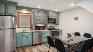 Une cuisine avec des armoires de couleur turquoise, des appareils en acier inoxydable et un coin repas comprenant une table en verre et des chaises noires.