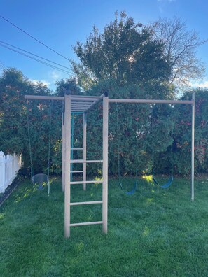 A wooden swing set with a ladder, surrounded by grass and trees.