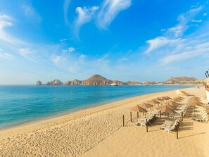 Une plage bordée de rangées de chaises longues et de parasols, un ciel bleu dégagé et une mer calme.