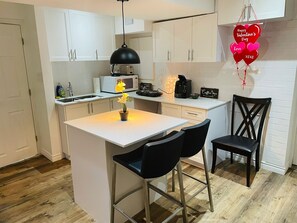 A modern kitchen with white cabinets, a black pendant light, a coffee machine, and a small island with two black chairs.
