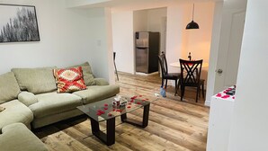 Una sala de estar con un sofá modular, una mesa de centro de vidrio adornada con pétalos de rosa y un comedor con una mesa y sillas.