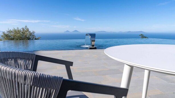 An infinity pool with a clear view of the ocean and mountains in the background, a white table, and black chairs. - Apartment Oliva Verdello - Maina Country Resort - with pool, in Sicily (Naso)