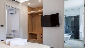 A modern hotel room with a bed, a TV mounted on the wall, a walk-in closet, and a bathroom with a glass shower. - Apartment Oliva Verdello - Maina Country Resort - with pool, in Sicily (Naso)