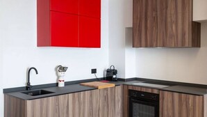 A modern kitchen with a black countertop, wooden cabinets, a red accent wall, a coffee maker, and a dishwasher. - Apartment Oliva Verdello - Maina Country Resort - with pool, in Sicily (Naso)