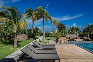 A poolside area with lounge chairs, a wooden deck, and palm trees.