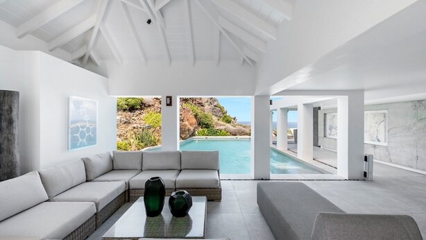 Um interior moderno com um sofá grande, uma mesa de centro e vista para uma piscina e paisagem rochosa.