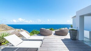 Um deck de madeira com espreguiçadeiras e assentos de vime com vista para o oceano.
