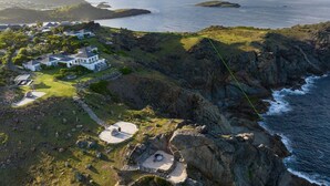 Vista aérea de una propiedad costera con varias casas, un litoral rocoso y una vista despejada del mar.