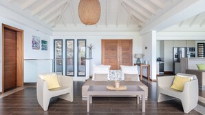 A modern living room with a dining table, two sofas, a large window, and a kitchen visible in the background. - Upside (2/3 Rooms) Luxury villa (Pointe Milou)