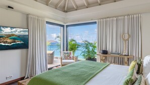 A bedroom with a bed, a chair, a table, and a view of the ocean. - Upside (2/3 Rooms) Luxury villa (Pointe Milou)