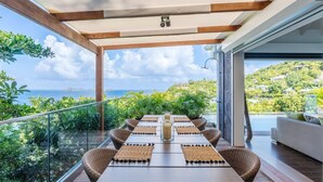A balcony with a table set for dining, overlooking a scenic ocean view. - Upside (2/3 Rooms) Luxury villa (Pointe Milou)