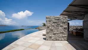 A infinity pool with a view of the sea, stone walls, and outdoor furniture.