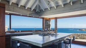 Une cuisine moderne dotée d’un grand îlot central, de grandes fenêtres et offrant une vue sur l’océan.
