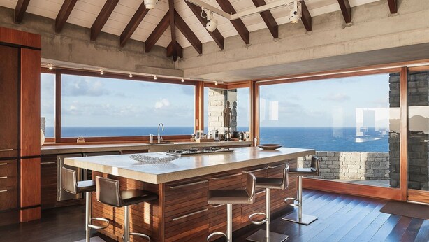 A kitchen with a large island, wooden bar stools, and a view of the sea.
