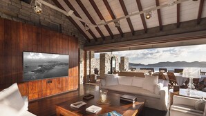 A spacious living room with a large TV, comfortable seating, and a view of the sea.