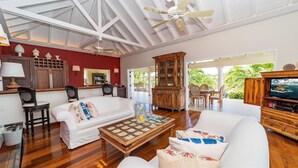 A spacious living area with a high ceiling, wooden flooring, and a large wooden cabinet. There is a white sofa with decorative pillows, a coffee table, and a television on a wooden stand. - Maracuja (1/3 Rooms) Luxury villa (Vitet)
