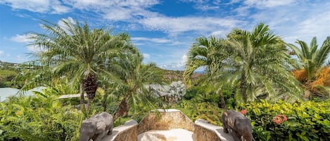 A tropical resort with palm trees, a stone water feature, and two elephant statues.
