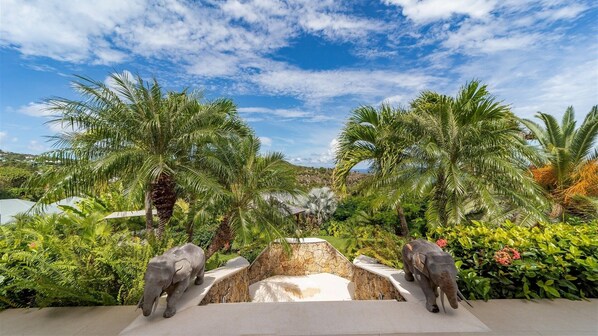 A tropical resort with palm trees, a stone water feature, and two elephant statues.