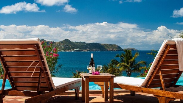 Two wooden lounge chairs facing a pool with a view of the sea and a mountainous landscape. - Alizee d'Eden (1/2 Rooms) (Pointe Milou)