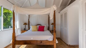 Uma cama de dossel com cortina, uma mesinha de cabeceira com abajur e vista para o exterior.